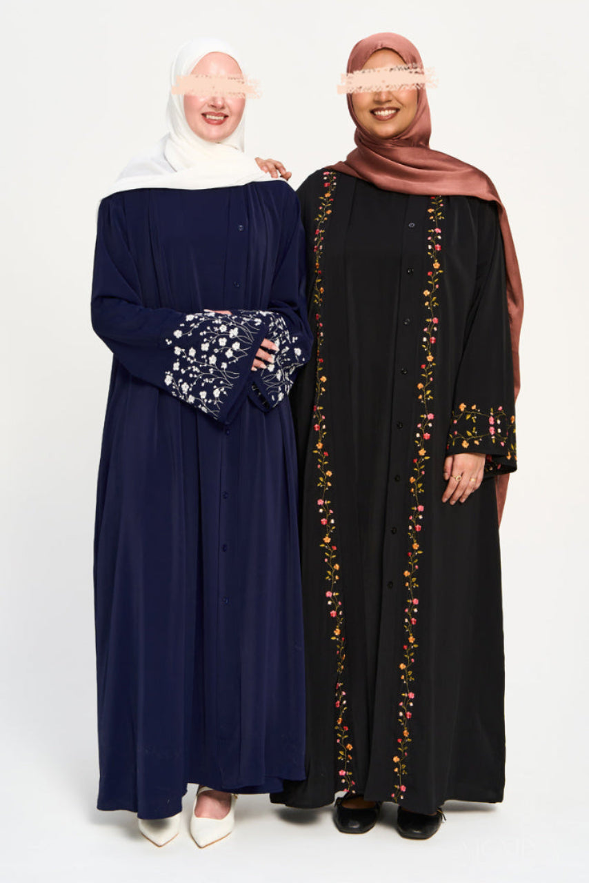 Two women wearing abayas, one navy and one black with floral details, on a white background.