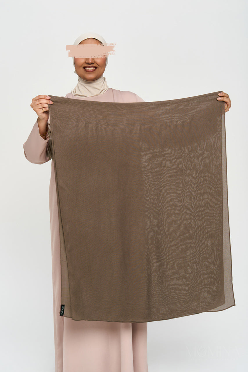 Muslim woman holding brown modal hijab on a white background by Momina Hijabs